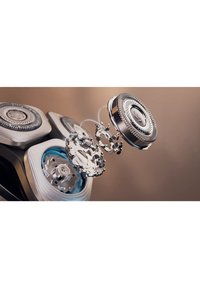 Elektrisch scheerapparaat hoofd gedemonteerd, met drie ronde messen, metalen zilverkleurige afwerking, gestructureerde oppervlakken en zichtbare interne mechanismen.