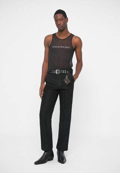 Sort mesh tanktop med tekst, parret med sorte teksturerede bukser. Har et sølvspænde bælte med øjer og sorte læder ankelstøvler.