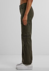 Pantaloni cargo verde oliva realizzati in cotone misto, dotati di tasche cargo laterali, una tasca con zip e una vestibilità dritta. Indossati con sneakers bianche.