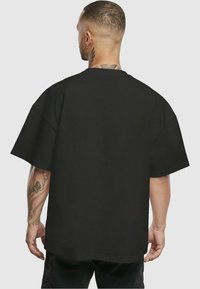Camiseta negra de gran tamaño hecha de algodón, con mangas cortas y cuello redondo. La parte trasera presenta un diseño liso y un ajuste relajado.