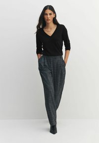 Pulover negru cu decolteu în V și pantaloni gri în carouri, cu talie înaltă, realizați dintr-un material neted, prevăzuți cu buzunare laterale și cu croială lejeră. Cizme negre cu toc.