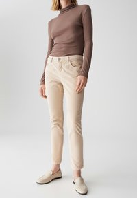 Beige corduroy broeken met een nauwsluitende pasvorm, voorzakken en een subtiele glans. Gepaald met een bruin shirt met lange mouwen en beige loafers.