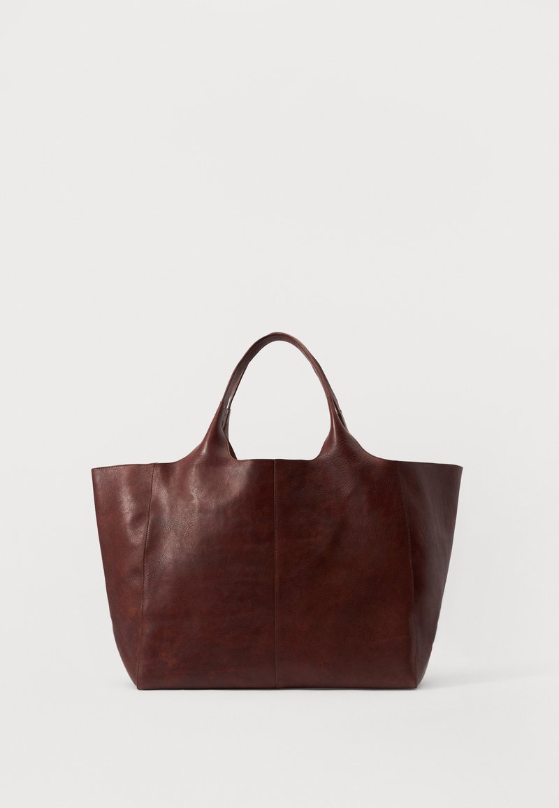 Barna bőr tote táska sima felülettel, széles testtel és két rövid fogantyúval. Minimalista varrással rendelkezik, látható hardver vagy díszítés nélkül.