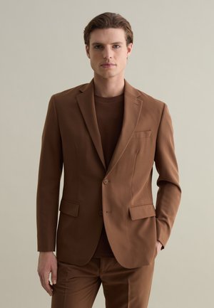 Blazer marrón de tela suave con dos botones, solapas con muesca y un bolsillo en el pecho, combinado con una camisa marrón a juego.