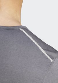 Szürke sportpóló sima textúrával és kerek nyakkivágással. Egy kontrasztos fehér varrás fut végig a vállvarráson.