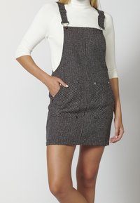 Svart och vit rutigt overallklänning med justerbara remmar, framfickor och en figursydd kjoldesign. Slät tygstruktur.