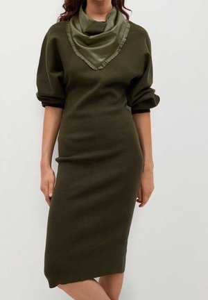 Femme portant une robe midi ajustée à manches longues vert olive avec une écharpe à franges assortie autour du cou.