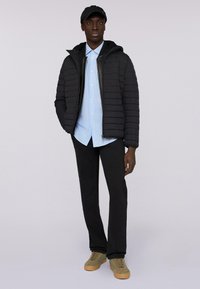 Svart puffjacka med horisontell quiltning, matchad med en ljusblå randig skjorta med knappar och svarta byxor, kompletterad med olivgröna skor.