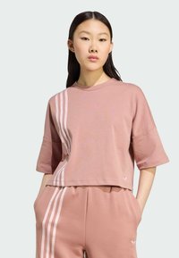 Ružový kratký tričko s krátkymi rukávmi, ktoré má biele vertikálne pruhy na jednej strane. Vyrobené z mäkkého materiálu s voľným strihom.