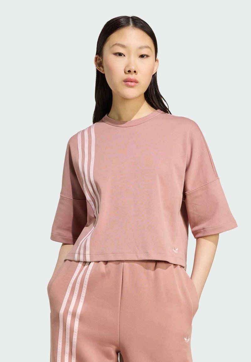 Ružový kratký tričko s krátkymi rukávmi, ktoré má biele vertikálne pruhy na jednej strane. Vyrobené z mäkkého materiálu s voľným strihom.