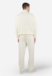 Hanorac moale, de culoare crem, cu guler înalt, purtat cu pantaloni jogger asortați. Ambele au manșete încrețite și o croială lejeră.
