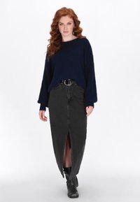 Navy Oversized-Strickpullover mit tiefen Schultern, kombiniert mit einem schwarzen Jeans-Maxikilt mit einem vorderen Schlitz, getragen mit schwarzen Stiefeletten.