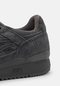 Sneaker in suede nero con finitura testurizzata, accenti più scuri in contrasto e dettaglio del logo sul lato. Presenta un collarino imbottito e suola in gomma.