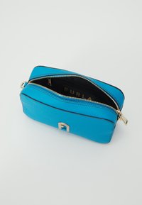 Tyrkysová kožená taštička se zlatými prvky, zipovým uzávěrem a černou podšívkou s logem. Obdélníkový tvar s texturovaným povrchem.