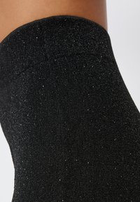 Collant neri glitterati con una texture a costine, caratterizzati da un aspetto lucido e metallico. Il tessuto presenta particelle d'argento sparse su tutta la superficie.