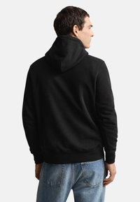 Sort hættetrøje med snor, der har en kængurulomme og ribbet manchetter. Bæreres med lyseblå denimjeans, der viser en afslappet pasform.