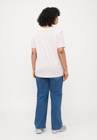 Light pink short-sleeve t-shirt with a rounded neckline, paired with loose-fitting blue jeans and gray sneakers. Back view shown.
