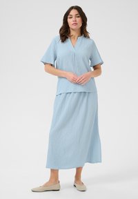 Lyseblå, struktureret top og nederdel i matchende sæt med korte ærmer og v-hals-design. Sammen med beige flade sko.