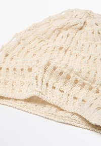Berretto lavorato a maglia in crema, caratterizzato da un motivo ad intaglio e una finitura testurizzata. Materiale morbido e leggero con una forma rilassata.