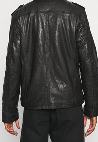 Zwarte leren jas met een gestructureerde afwerking, zichtbare stiksels en schouderepauletten. Heeft een rechte snit en lange mouwen.