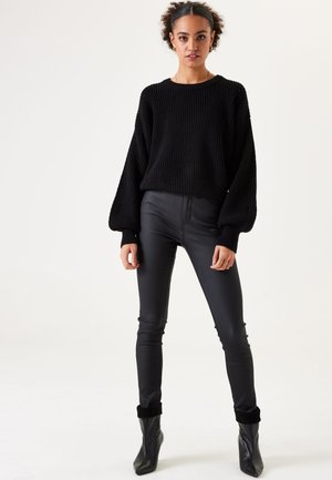 Zwarte gebreide trui met oversized mouwen, gecombineerd met hoog design zwarte leren broeken en stijlvolle zwarte enkellaarsjes. Glad textuur, aansluitend ontwerp.