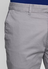 Pantaloni grigi chiari realizzati in un mix di cotone, con una texture liscia, tasche tradizionali e un design a vita piatta.