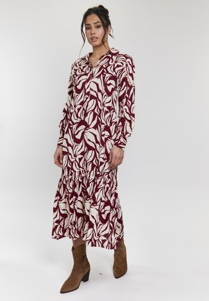 Langærmet kjole med et maroon og off-white bladmønster, krave og flæsefor. Båret med brune ruskinds ankelstøvler.