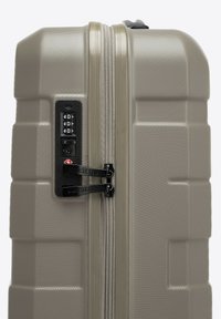 Valigia rigida di colore grigio chiaro con una finitura texturizzata. Presenta due tiranti neri per la cerniera e una serratura a combinazione sul lato.