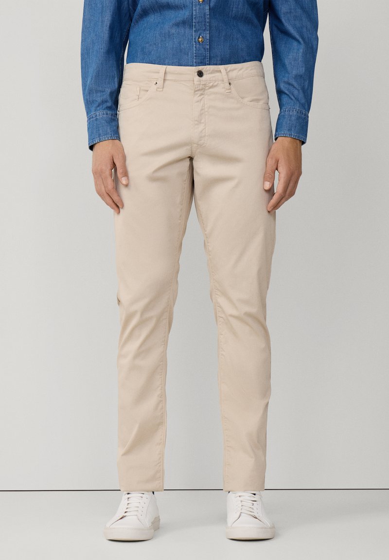 Beige chino broek in een slim fit stijl, gemaakt van katoen, met voorzakken, achterzakken en een knoopsluiting. Draagt met witte sneakers.