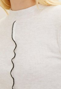 Jasnoszary, prążkowany sweter z wysokim kołnierzem i kontrastującymi, czarnymi, falistymi detalami na przodzie, wykonany z miękkiego, teksturowanego materiału.