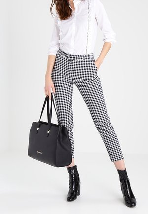 Černá taška přes rameno se zlatými doplňky, doplněná o vysoce pasované černobílé kostkované kalhoty a černé boty na podpatku. Outfit doplňuje bílá košile.