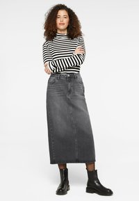 Grauer Denim-Maxikleid mit Fronttaschen, kombiniert mit einem schwarz-weißen gestreiften Langarmoberteil und schwarzen Lederstiefeletten.