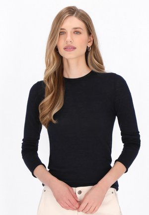 Maglietta a maniche lunghe blu navy realizzata in un tessuto leggero e testurizzato. Presenta un collo a giro e una silhouette aderente, abbinata a pantaloni bianchi.