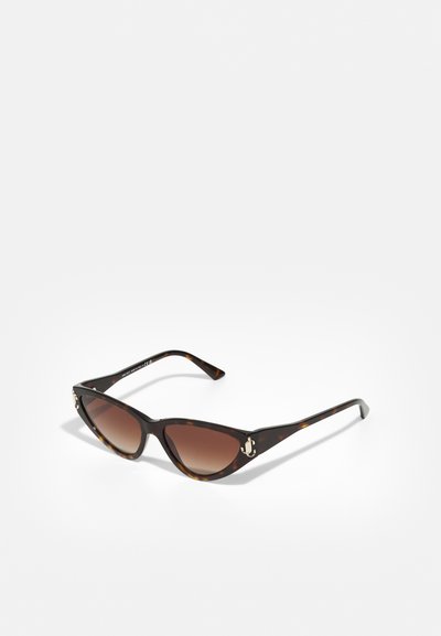 Lunettes de soleil en écaille de tortue avec une forme œil de chat, verres dégradés marron et accents dorés sur les côtés. Monture en plastique élégante.