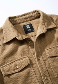 Camicia in velluto a coste marrone con colletto, due tasche sul petto e chiusura con bottoni. Tessuto testurizzato con strisce verticali. Etichetta del marchio visibile.