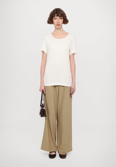 White short-sleeve t-shirt paired with beige wide-leg pants, holding a small dark handbag. Simple design, soft texture, relaxed fit.