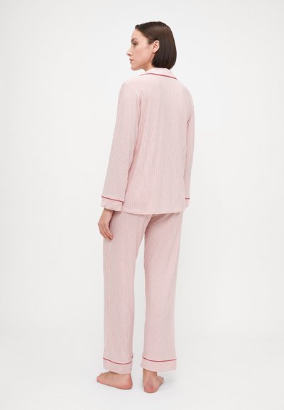 Conjunto de pijama com riscas vermelhas e brancas, com mangas compridas e calças. Apresenta um colarinho, um bolso no peito e um acabamento vermelho em contraste nos punhos.