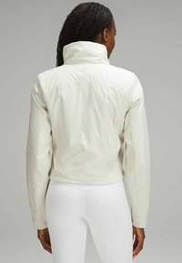 Biała, lekka kurtka z wysokim kołnierzem, o gładkiej fakturze i żebrowanych bocznych panelach, prezentująca widok z tyłu na jednolitym tle.