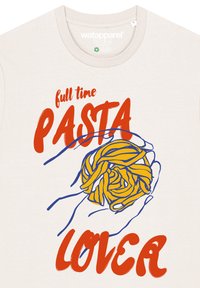 T-shirt en coton beige clair avec des mains contournées de bleu tenant des pâtes jaunes, portant le texte rouge : "amateur de PÂTES à plein temps" en caractères gras.