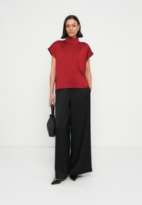 Punainen lyhythihainen paita korkealla kauluksella, yhdistetty mustiin leveälahkeisiin housuihin, pieneen mustaan käsilaukkuun, tasapohjaisiin kenkiin ja minimalistiseen yksityiskohtaisuuteen.