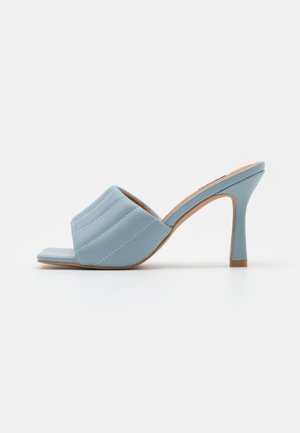 Zuecos de tacón alto en azul claro con diseño acolchado y acolchonado y puntera abierta. Presentan un tacón estilizado y una textura suave con costuras contrastantes.