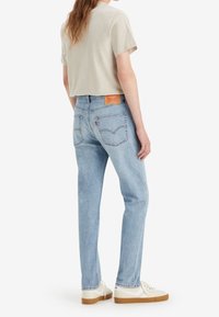 Ljusgrå kort t-shirt i kombination med ljusblå denimjeans, med en brun läderpatch bak och vita sneakers med gummisulor.