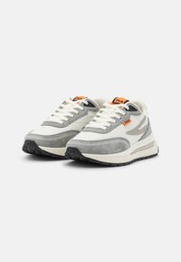 Paire de baskets FILA blanches et grises avec des accents orange et des semelles noires, légèrement inclinées vers la droite sur un fond blanc.