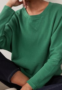 Haut vert en tricot gaufré à manches longues avec un décolleté en V et une coupe décontractée, doté de poignets côtelés et d'une surface texturée.