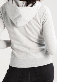 Sudadera gris con una textura suave, presenta una capucha con cordón y puños acanalados, se ajusta cómodamente en la cintura, fabricada con material ligero.
