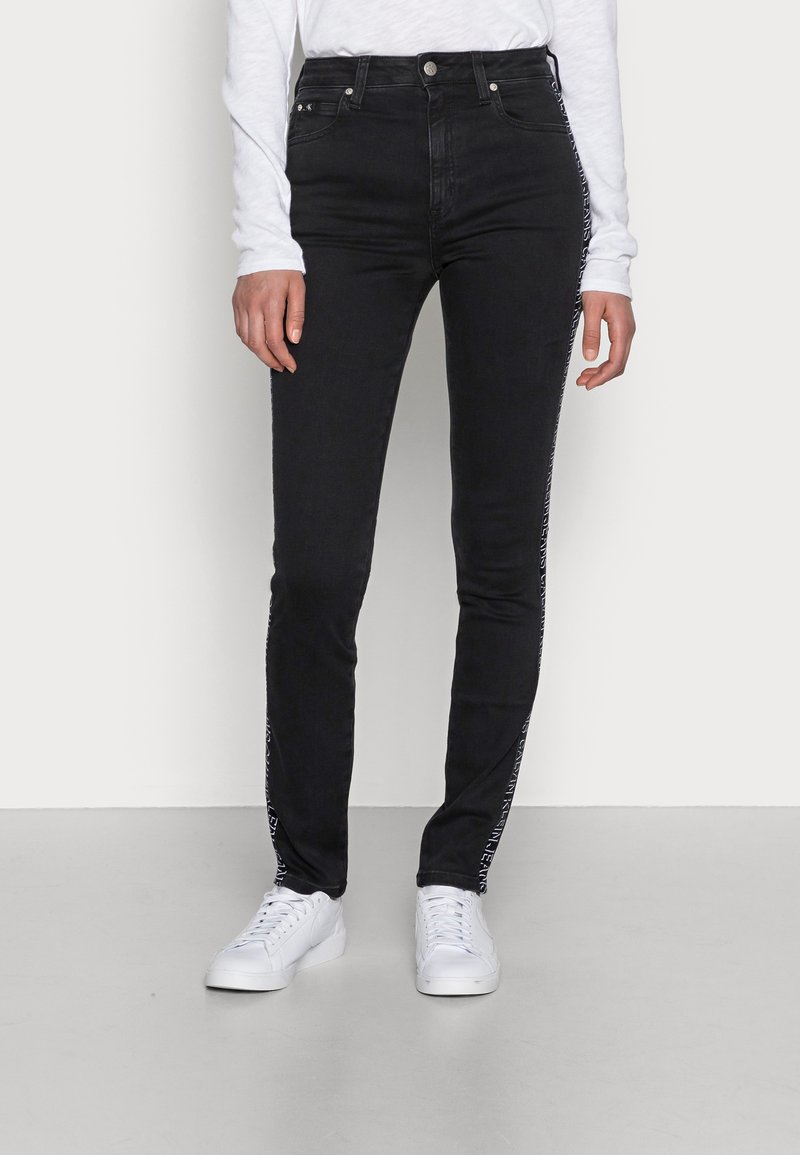 Jeans skinny negros con detalles en blanco a lo largo del costado, hechos de denim elástico, con una cintura alta y un diseño clásico de cinco bolsillos.