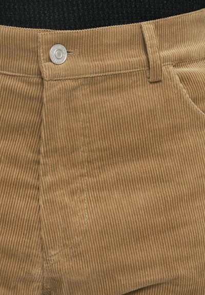 Brune kordfløjspants med lodrette striber, med en metalknap i taljen og detaljeret syning langs lommer og sømme.