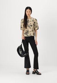 Beige topp med svart blomstertrykk, korte puff-ermer; kombinert med tettsittende svarte bukser og svarte åpne blokkhelsandaler. Svart håndveske.