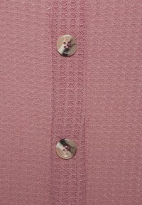 Knopen-up cardigan in zachte roze stof, met een textuur breipatroon en een ronde, glanzende knoop met contrasterend garen.