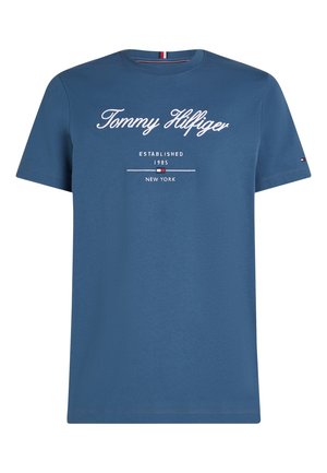 Μπλε κοντομάνικη μπλούζα με το κείμενο "Tommy Hilfiger", ιδρύθηκε το 1985, Νέα Υόρκη, και ένα μικρό λογότυπο στο αριστερό μανίκι.